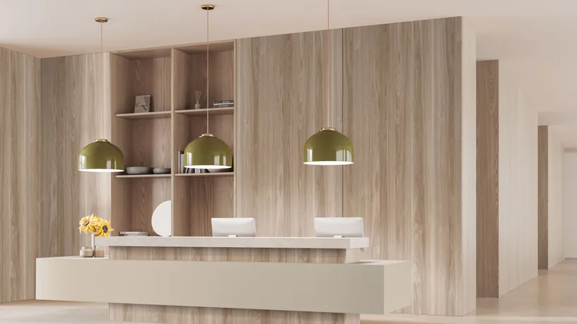 Drewniano-kaszmirowa recepcja wykonana z płyty ognioodpornej laminowanej od Woodeco, wyposażona w dwa komputery, wiszące zielone lampy oraz regał w minimalistycznym lobby biurowym.